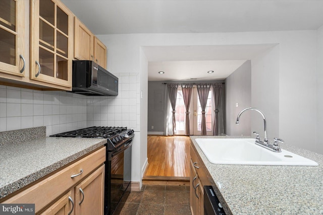 kitchen with black appliances, a sink, backsplash, light countertops, and glass insert cabinets