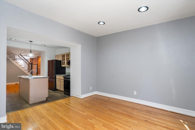 kitchen with black appliances, baseboards, light wood-type flooring, and a sink