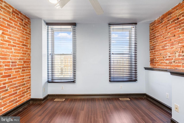 spare room featuring visible vents, wood finished floors, baseboards, and brick wall