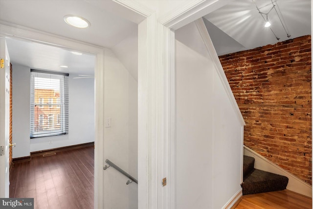 corridor with baseboards, wood finished floors, brick wall, and stairs