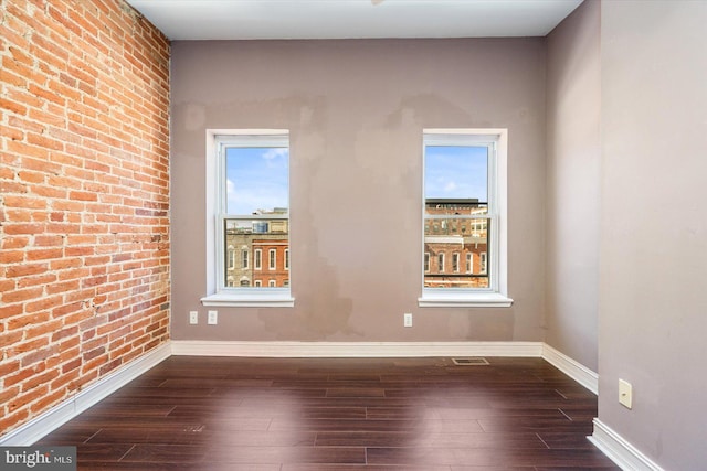 empty room featuring dark wood-style floors, brick wall, and baseboards