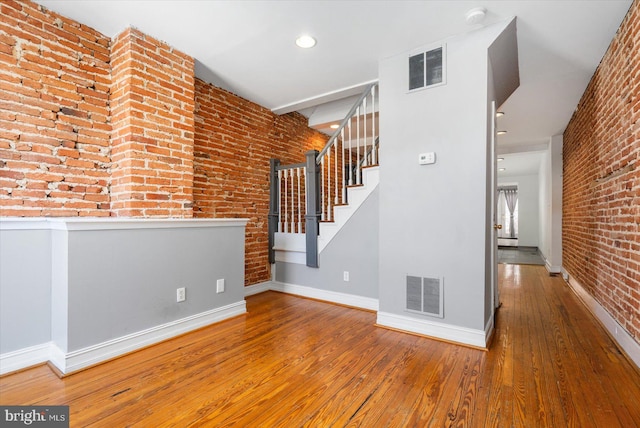 interior space featuring visible vents, brick wall, baseboards, and hardwood / wood-style flooring