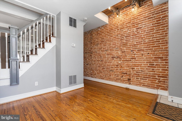 spare room featuring hardwood / wood-style floors, visible vents, baseboards, and brick wall