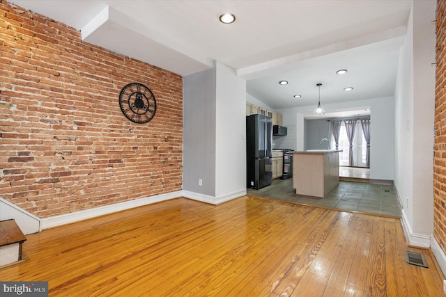 unfurnished living room with visible vents, baseboards, brick wall, a sink, and light wood-type flooring