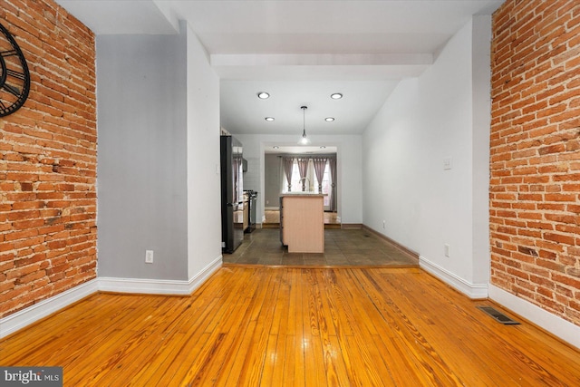 unfurnished dining area featuring light wood-style flooring, baseboards, visible vents, and brick wall