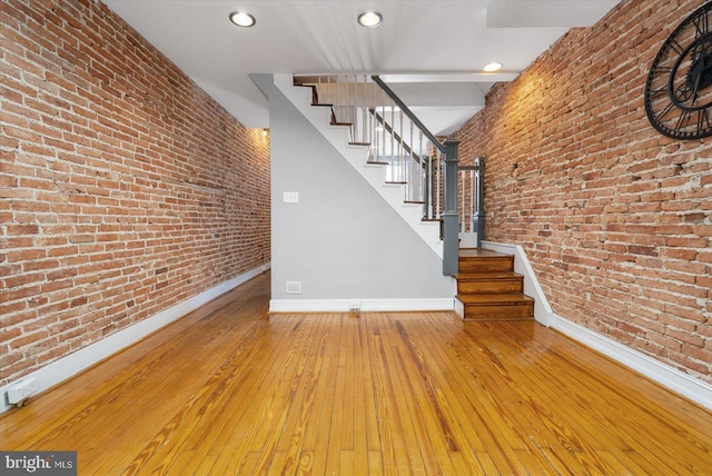 stairs featuring wood-type flooring, recessed lighting, baseboards, and brick wall