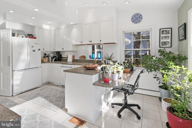 kitchen featuring dark countertops, white appliances, a peninsula, white cabinets, and light tile patterned floors