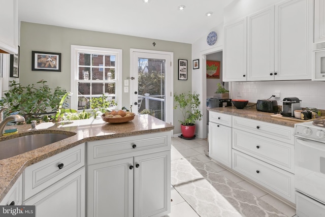 kitchen with white appliances, light stone counters, a sink, white cabinetry, and backsplash