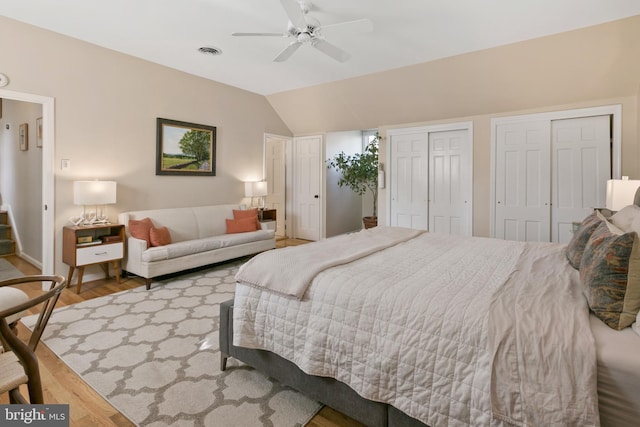 bedroom featuring wood finished floors, visible vents, ceiling fan, vaulted ceiling, and two closets