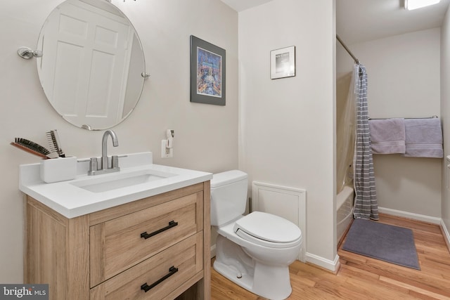 full bath with toilet, shower / tub combo with curtain, wood finished floors, baseboards, and vanity