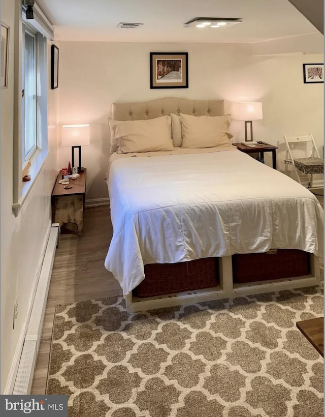 bedroom featuring visible vents, baseboards, wood finished floors, and a baseboard heating unit