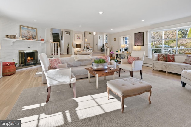 living room with a brick fireplace, recessed lighting, baseboard heating, and light wood finished floors