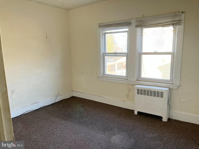 unfurnished room with radiator heating unit, baseboards, and dark carpet