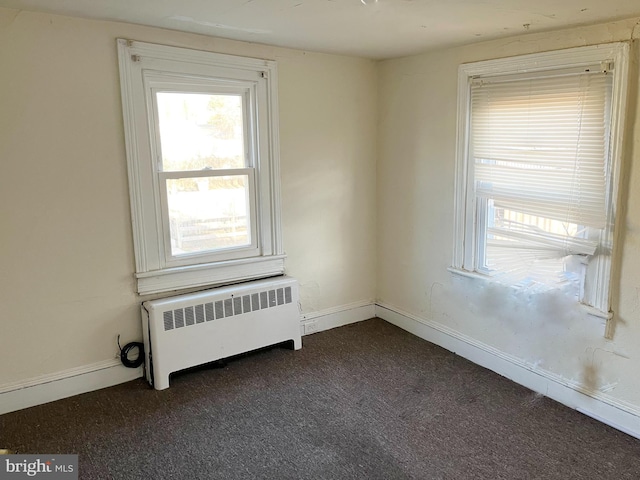 empty room featuring radiator heating unit, baseboards, and dark colored carpet