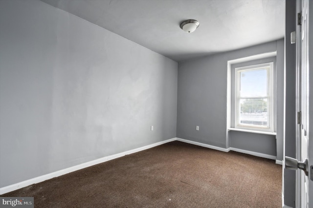 unfurnished room with dark colored carpet and baseboards