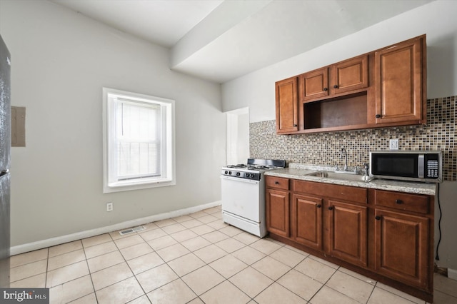 kitchen with a sink, stainless steel microwave, light tile patterned floors, decorative backsplash, and white gas range