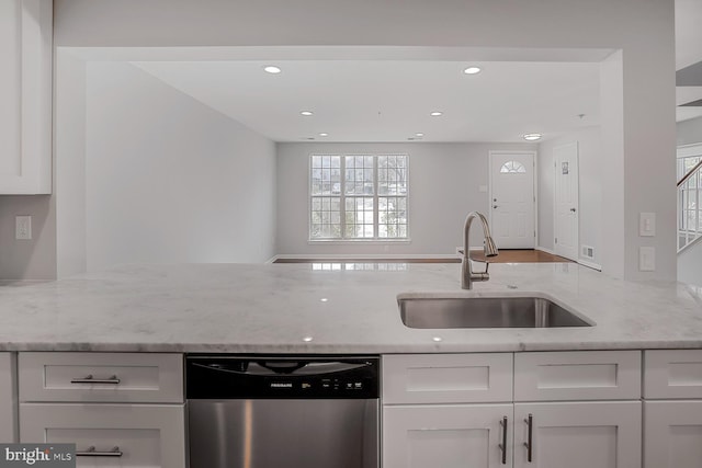 kitchen with a sink, light stone counters, stainless steel dishwasher, and white cabinetry