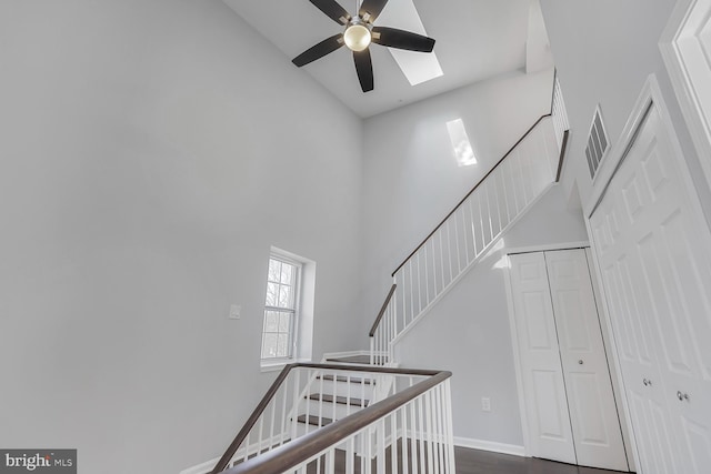 staircase with visible vents, a ceiling fan, wood finished floors, baseboards, and a towering ceiling