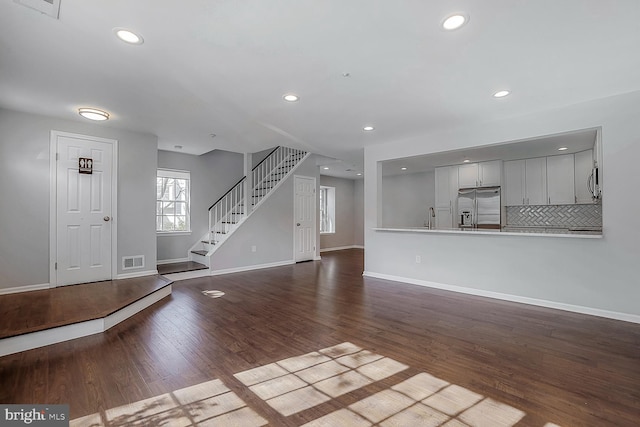 unfurnished living room with wood finished floors, visible vents, recessed lighting, a sink, and stairs