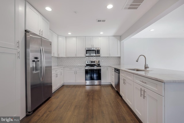 kitchen with visible vents, light stone countertops, appliances with stainless steel finishes, a peninsula, and a sink