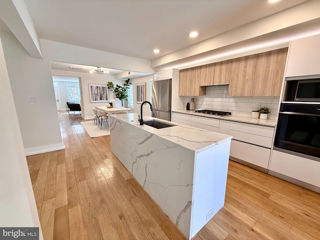 kitchen with modern cabinets, a sink, light wood-style floors, appliances with stainless steel finishes, and decorative backsplash