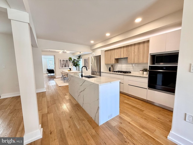 kitchen with modern cabinets, a kitchen island with sink, a sink, stainless steel appliances, and light wood-style floors