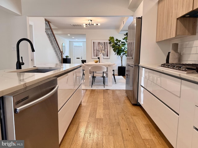 kitchen featuring light wood-type flooring, modern cabinets, a sink, backsplash, and stainless steel appliances