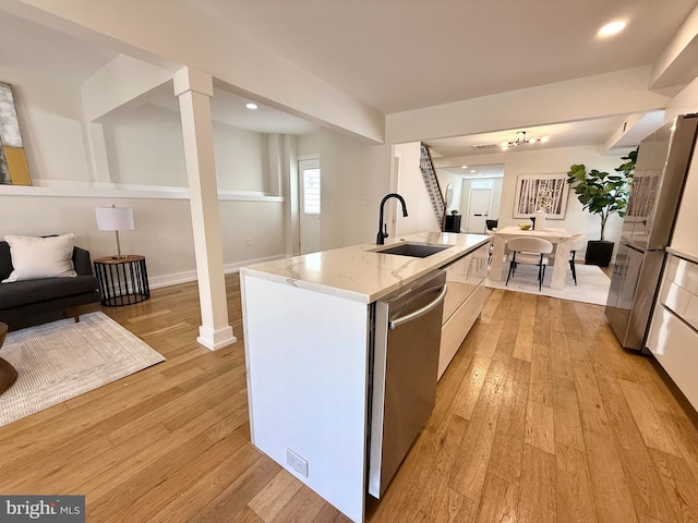 kitchen with light stone counters, light wood-style flooring, a sink, stainless steel dishwasher, and open floor plan