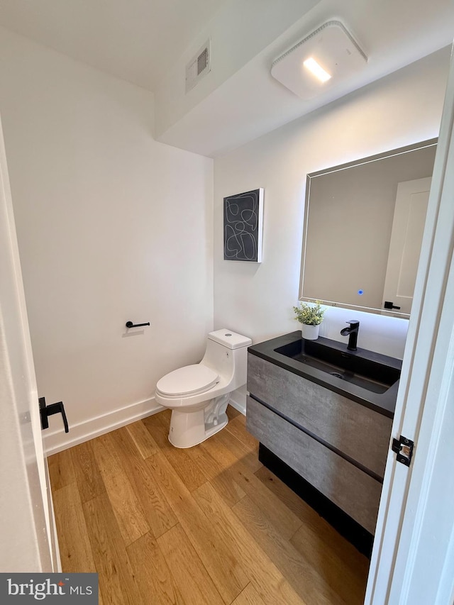 half bath featuring vanity, wood finished floors, visible vents, baseboards, and toilet