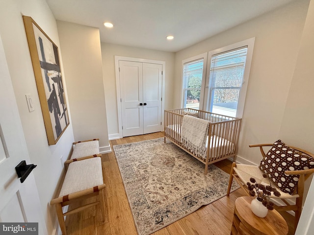 bedroom with baseboards, recessed lighting, wood finished floors, a closet, and a nursery area