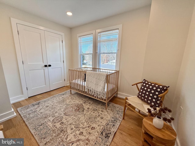 bedroom with recessed lighting, a nursery area, wood finished floors, and baseboards