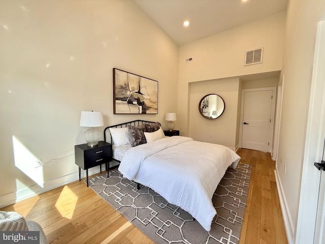 bedroom with wood finished floors, visible vents, baseboards, a high ceiling, and recessed lighting