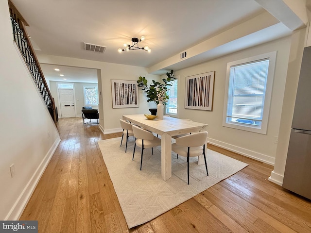 dining space featuring visible vents, light wood-style floors, a healthy amount of sunlight, and stairs