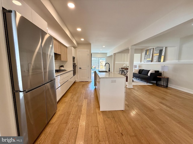 kitchen with a sink, light countertops, light wood-style floors, appliances with stainless steel finishes, and modern cabinets