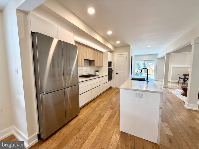 kitchen with a sink, decorative backsplash, light wood-style floors, appliances with stainless steel finishes, and modern cabinets