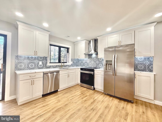 kitchen featuring wall chimney range hood, light countertops, light wood-style floors, white cabinets, and stainless steel appliances