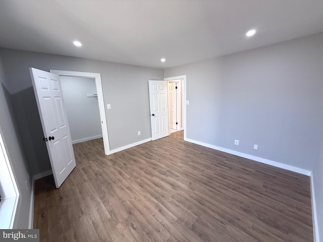 unfurnished bedroom with recessed lighting, a walk in closet, baseboards, and wood finished floors