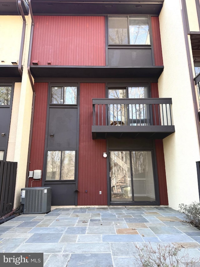 property entrance with central AC unit, a balcony, and stucco siding