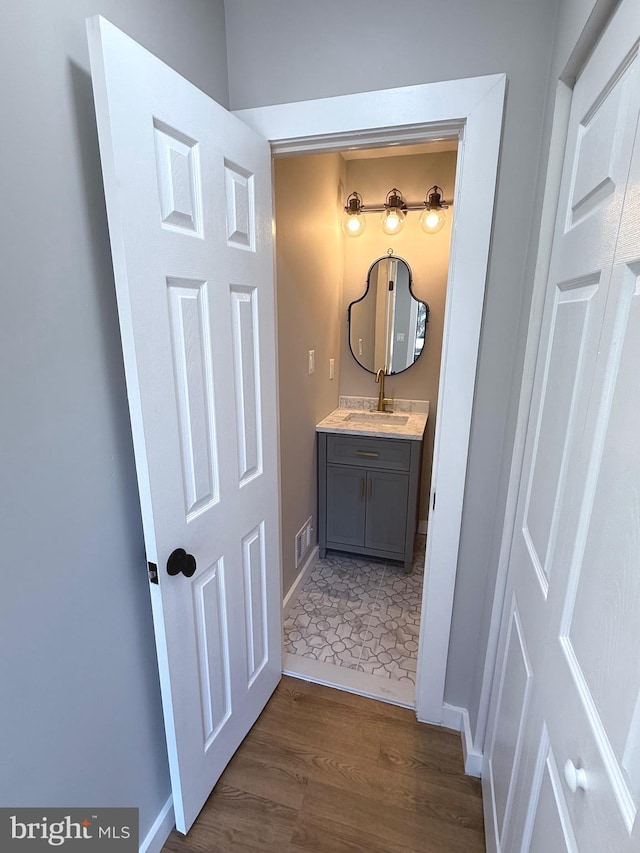 hall featuring a sink, visible vents, baseboards, and dark wood finished floors