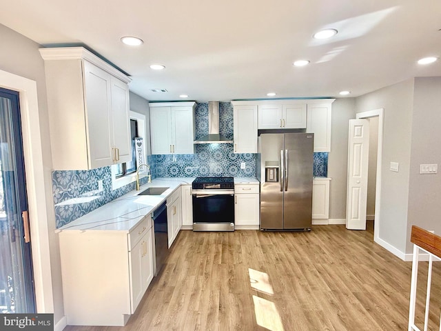 kitchen featuring wall chimney range hood, light wood-style flooring, stainless steel appliances, white cabinetry, and a sink