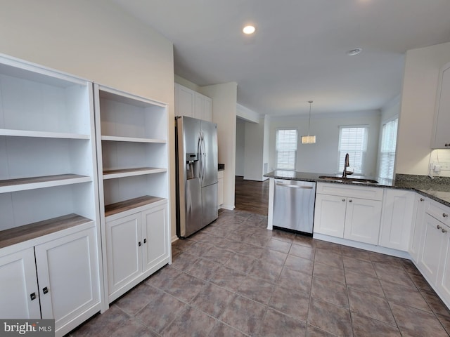 kitchen with a sink, dark stone countertops, stainless steel appliances, a peninsula, and white cabinets