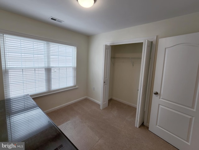 unfurnished bedroom featuring a closet, visible vents, light colored carpet, and baseboards