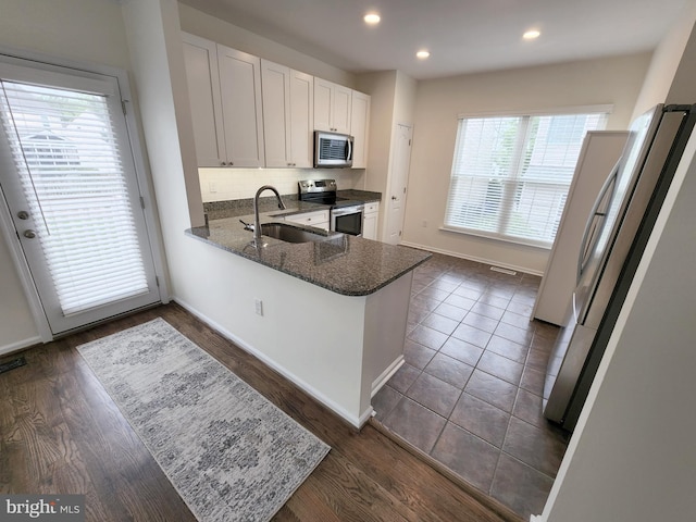 kitchen featuring backsplash, dark wood finished floors, dark stone countertops, appliances with stainless steel finishes, and a sink