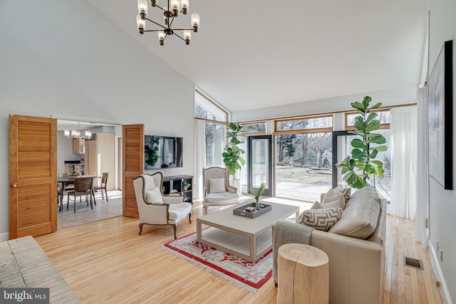 living area featuring visible vents, baseboards, a chandelier, light wood-style flooring, and high vaulted ceiling