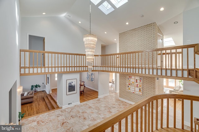 stairs with baseboards, a skylight, an inviting chandelier, wood finished floors, and high vaulted ceiling