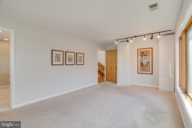 spare room featuring visible vents, baseboards, light colored carpet, stairs, and rail lighting