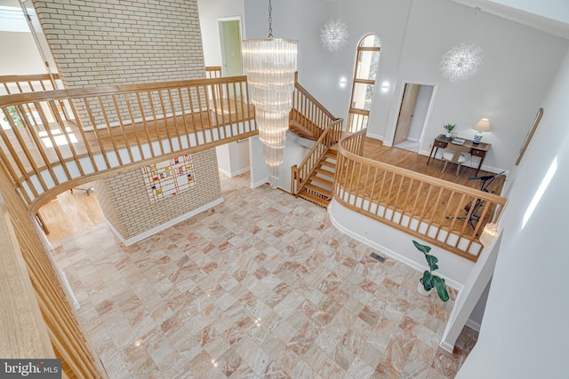 stairs featuring a chandelier, brick wall, baseboards, and a towering ceiling