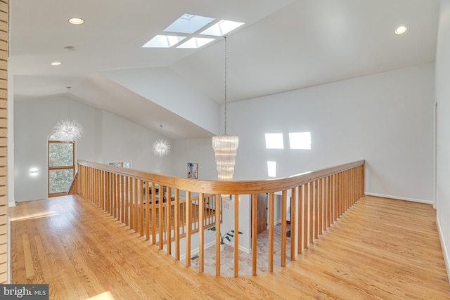 corridor with a chandelier, lofted ceiling with skylight, an upstairs landing, recessed lighting, and wood finished floors