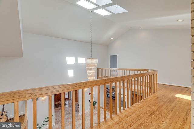 hall featuring an upstairs landing, recessed lighting, vaulted ceiling with skylight, an inviting chandelier, and wood finished floors