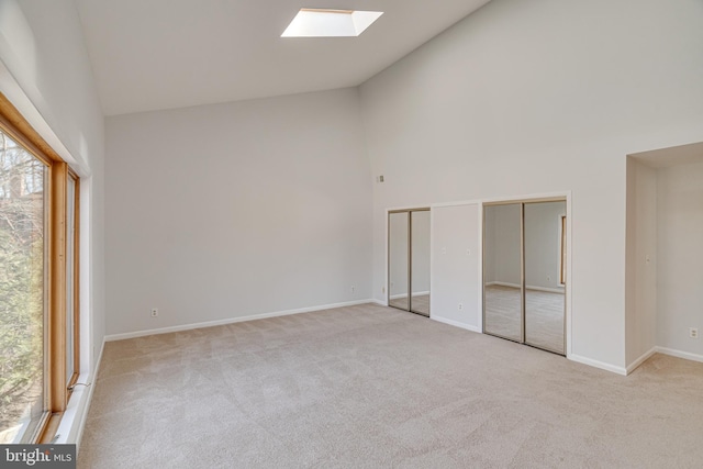 unfurnished room with baseboards, high vaulted ceiling, a skylight, and carpet